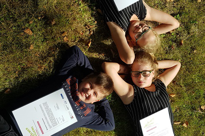 Drei Kinder aus dem Projekt liegen mit den Köpfen aneinander im Gras