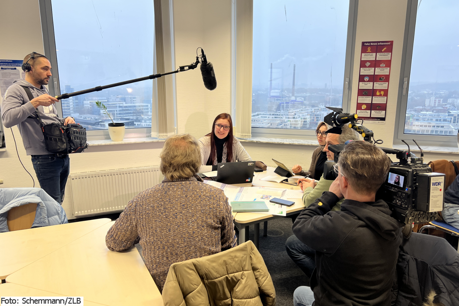 Eine Frau sitzt am Tisch, umgeben von einem Kamerateam